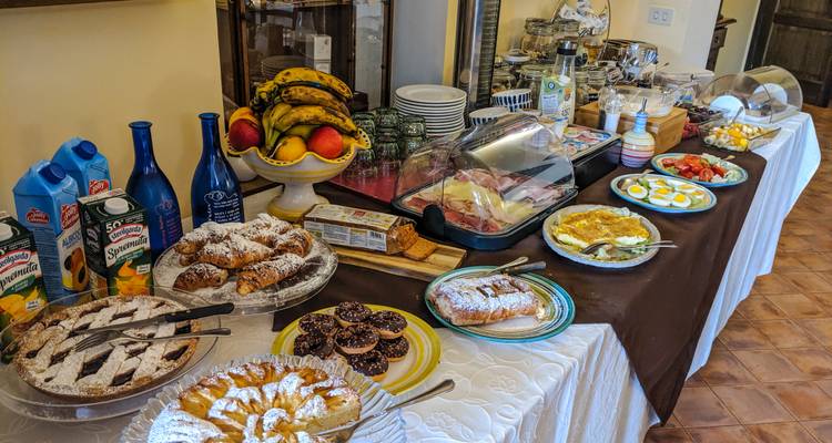 Buffet de petit-déjeuner garni de viennoiseries, fruits, œufs et charcuterie dans un espace de restauration rustique.