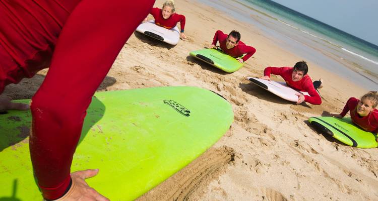 Surflehrerin demonstriert Paddeltechnik an Studenten im Sand mit leuchtend grünen Boards.