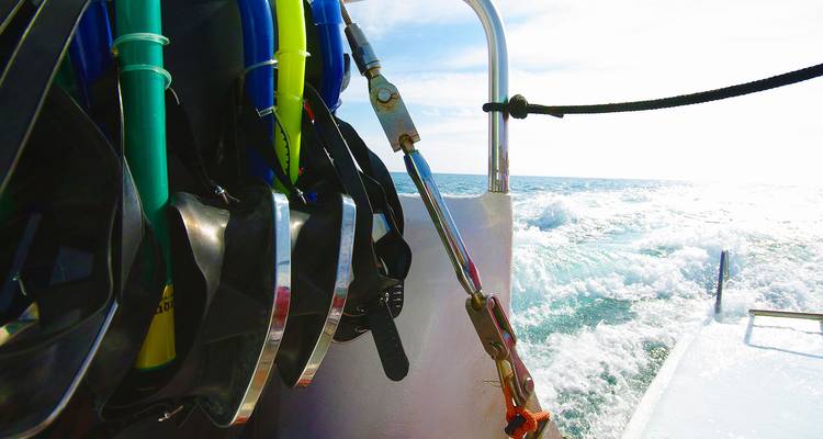 Snorkeluitrusting en duikvinnen hangen aan de reling van een boot terwijl het schip over de helderblauwe zee voortsnelt.