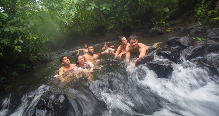 Een groep vrienden ontspant zich in een dampende jungle natuurlijke warmwaterbron met water dat erlangs stroomt.
