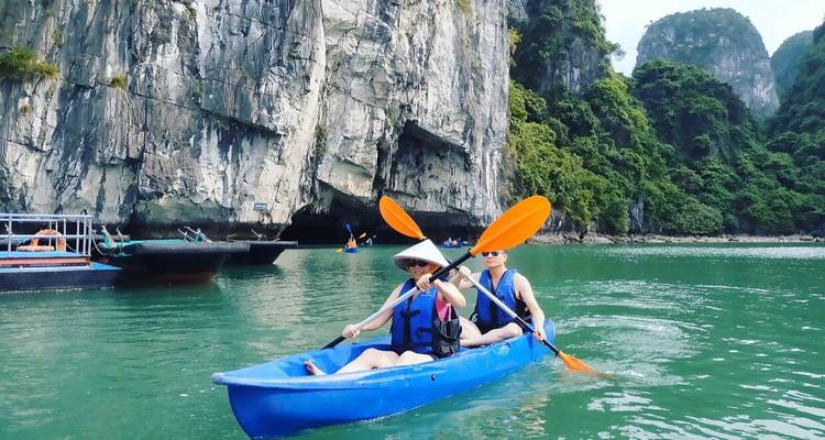 Twee mensen aan het kajakken op een groen wateroppervlak met kliffen op de achtergrond.