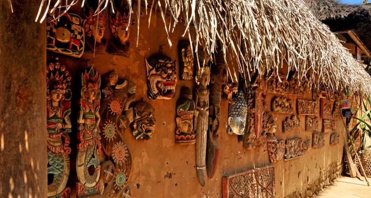 Wand eines traditionellen Dorfhauses, geschmückt mit kunstvoll geschnitzten Holzmasken und -tafeln.