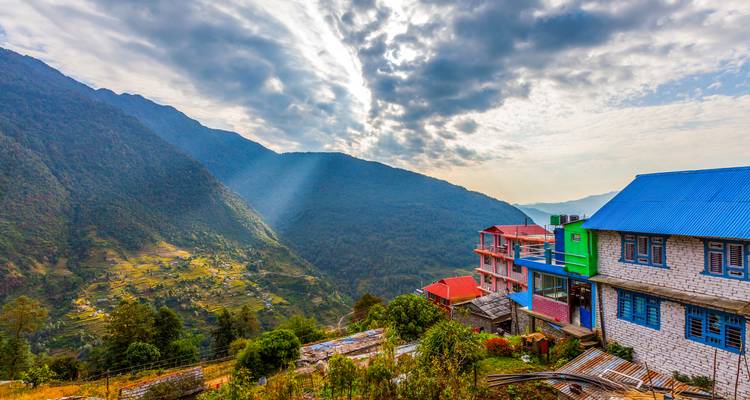 Des rayons de soleil percent des nuages dramatiques au-dessus de terrasses en damier et de lodges colorés à flanc de colline.