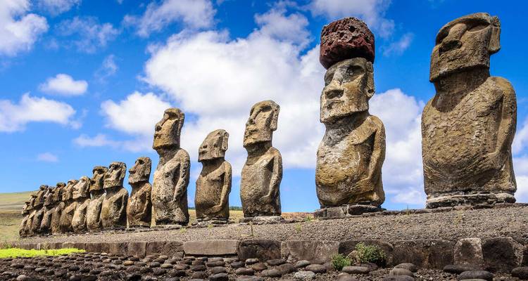 Rij van Moai-beelden op een stenen platform onder een blauwe hemel.