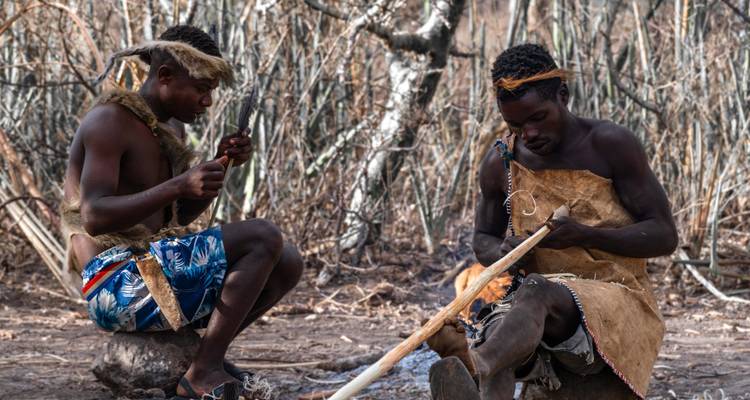 Zwei Männer stellen Werkzeuge in einem bewaldeten Gebiet her.