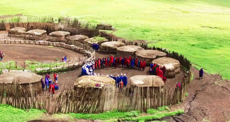 Traditionelles Maasai-Dorf mit runden Hütten und sich versammelnden Menschen.