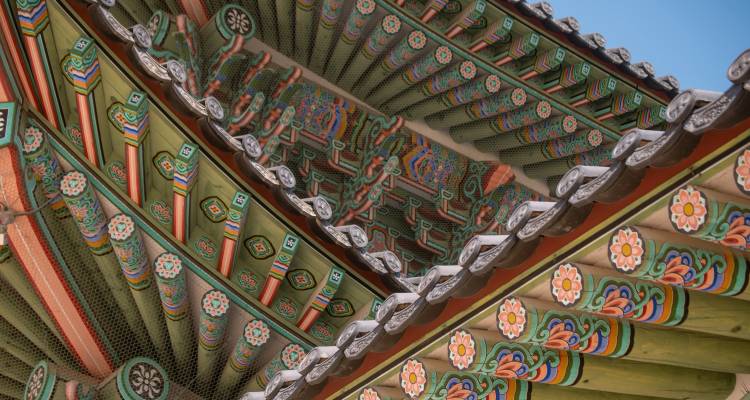 Vue détaillée des avant-toits en bois peints de couleurs vives d'un toit de palais coréen traditionnel contre un ciel bleu dégagé