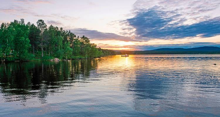 A sunset view over a calm lake with trees.