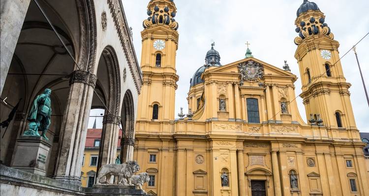 Une église jaune historique avec de grandes colonnes et des statues, se détachant sur un ciel nuageux.