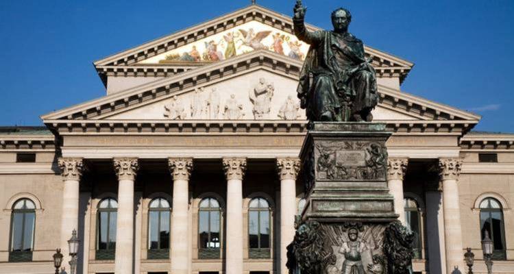 Un bâtiment historique avec une grande statue devant, sous un ciel bleu.