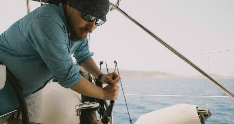 Marin en bandana ajustant les cordages sur un yacht avec une toile de fond d'eau bleue.