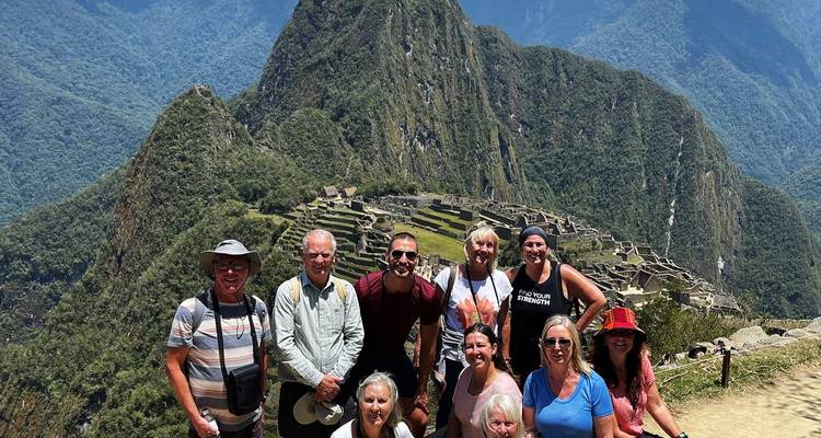 Lächelnde Reisegruppe, die am klassischen Aussichtspunkt oberhalb der antiken Steinzitadel von Machu Picchu mit üppigen Gipfeln im Hintergrund posiert