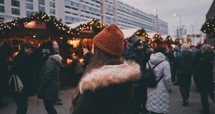Een vrouw in een bontjas en oranje muts die naar een kerstmarkt kijkt.