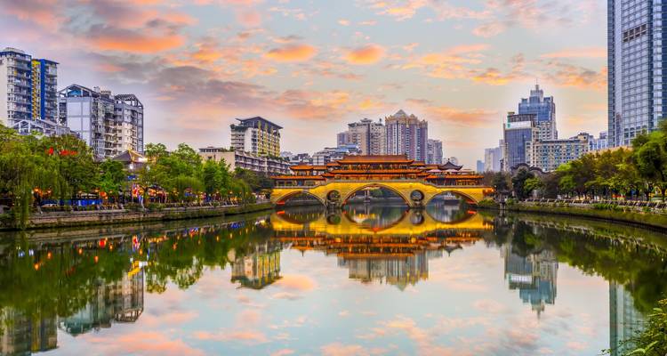 Un puente decorativo sobre un río con el horizonte de la ciudad y el cielo del atardecer.