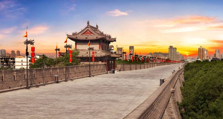 Oude stadsmuur die leidt naar een paviljoen bij zonsondergang.