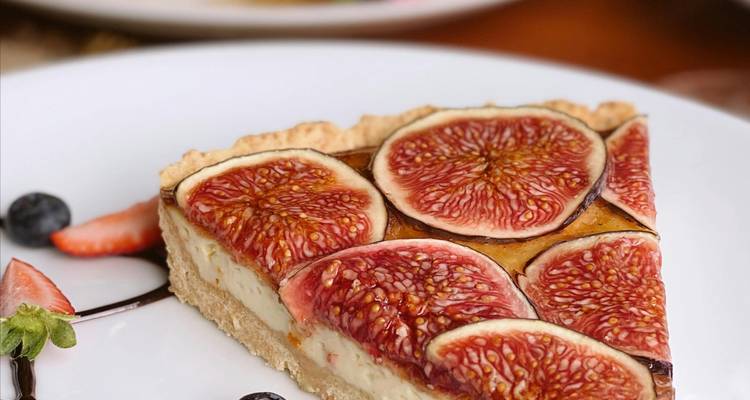 Gros plan d'une part de tarte aux figues dans une assiette blanche, joliment garnie de baies et de filet de chocolat.