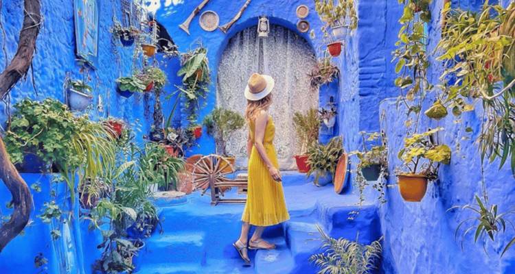 Frau in gelbem Kleid, die in den blauen Straßen von Chefchaouen steht.