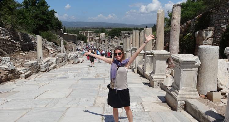 Smiling traveler posing with arms raised among ancient marble columns in Ephesus