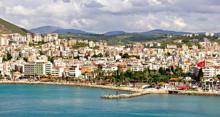 Seaside cityscape of Kusadasi with mountains in the background and Turkish flags