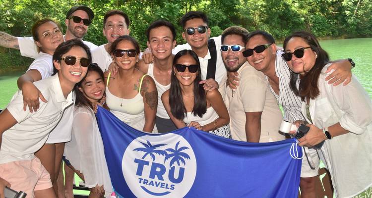 Grupo de personas posando con una bandera de TRU Travels en un río.