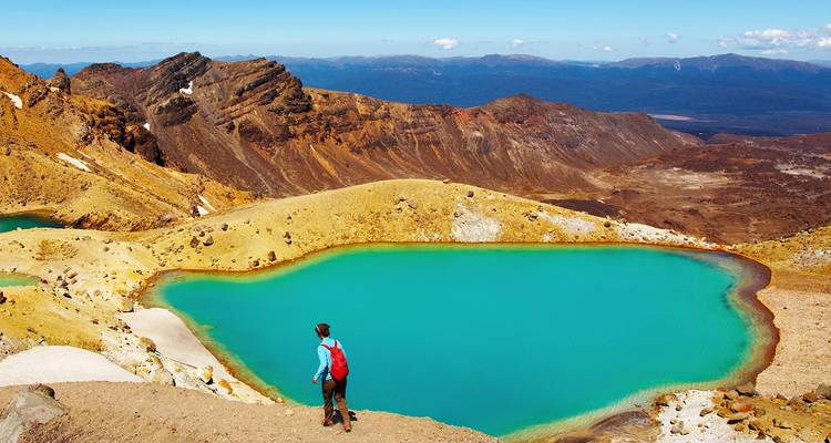 Wandelaar met rode rugzak kijkt uit over het levendige turquoise Emerald Lake in het Tongariro Alpenlandschap