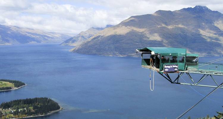 La plataforma de swing de Nevis sobresale sobre un lago azul y montañas escarpadas con un amante de las emociones preparándose para saltar.