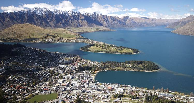 Spektakuläre Luftaufnahme von Queenstown neben dem tiefblauen Lake Wakatipu mit schneebedeckten Bergen im Hintergrund.