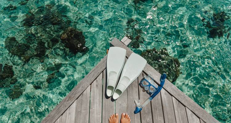 Ein Paar Schnorchelflossen und -ausrüstung auf einem Holzsteg über klarem Wasser.