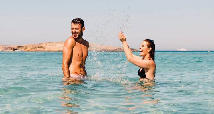 Smiling couple splashing water in a clear turquoise sea on a sunny beach day.