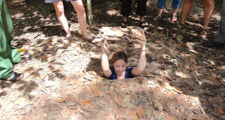Traveller lowers herself into a small tunnel hidden beneath dry leaves at the Cu Chi historic site