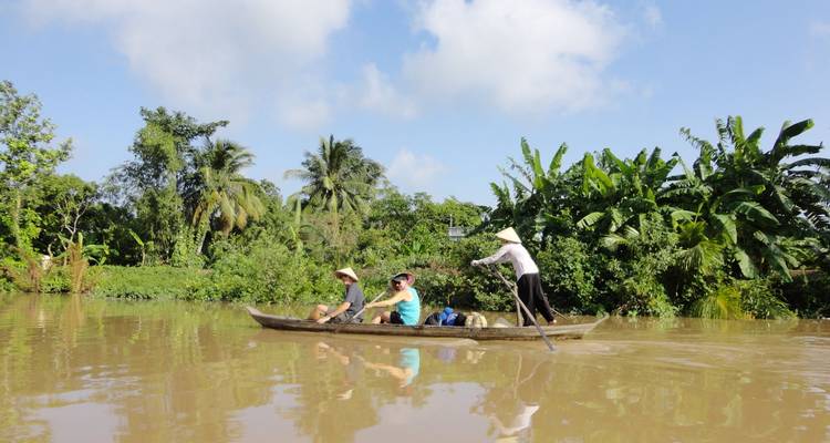 Un batelier local faisant naviguer des touristes à la pagaie dans un canal de jungle boueux bordé de palmiers luxuriants dans le delta du Mékong au Vietnam.