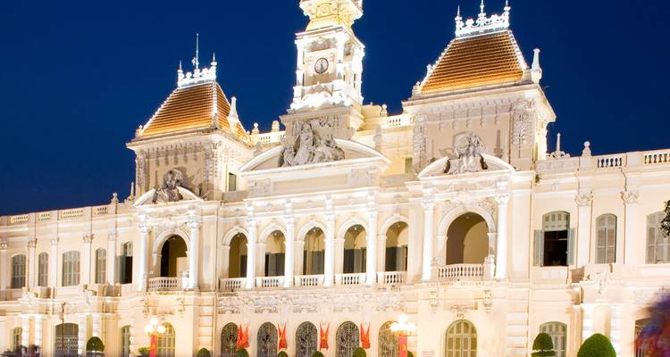 Majestueux Hôtel de Ville colonial de Ho Chi Minh-Ville illuminé d'une lumière chaleureuse contre un ciel de soirée profond.