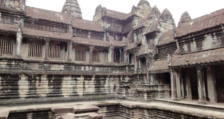 Cour intérieure usée par les intempéries d'Angkor Wat avec ses galeries de pierre sombre et ses piliers sous une lumière voilée.