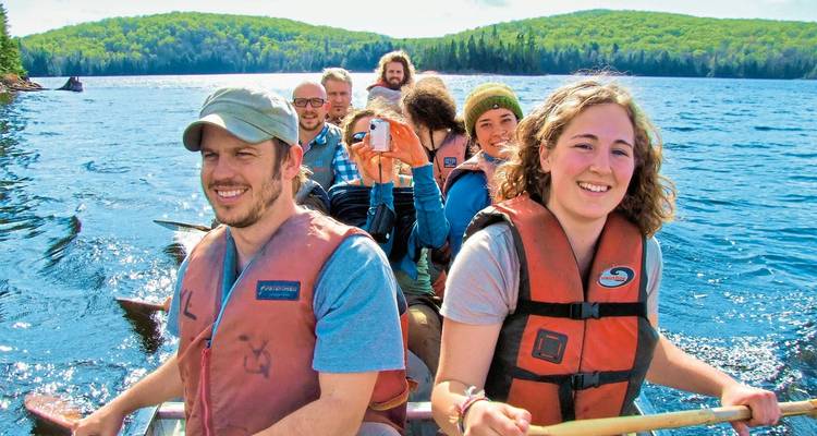 Grupo de amigos navegando en canoa en un lago con un frondoso bosque de fondo.