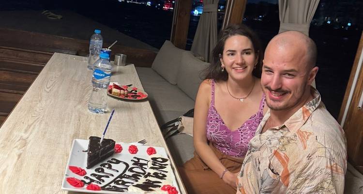 Glimlachend stel dat aan boord een verjaardag viert met taart en de jachthaven op de achtergrond in de nacht.