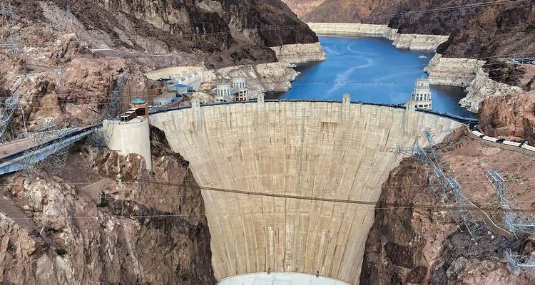 Massive curved concrete wall of Hoover Dam holding back blue reservoir water