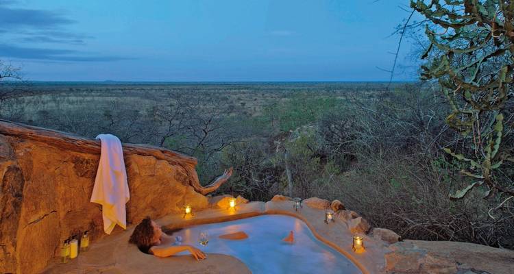 Personne se détendant dans une piscine naturelle au coucher du soleil à la lueur des bougies.