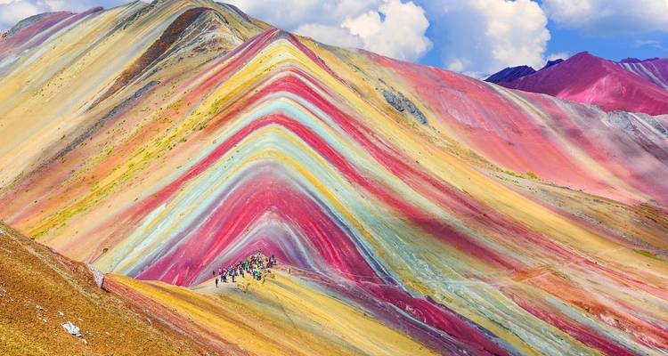 Las vibrantes laderas estriadas de la Montaña Arcoíris con pequeños senderistas en la cresta.