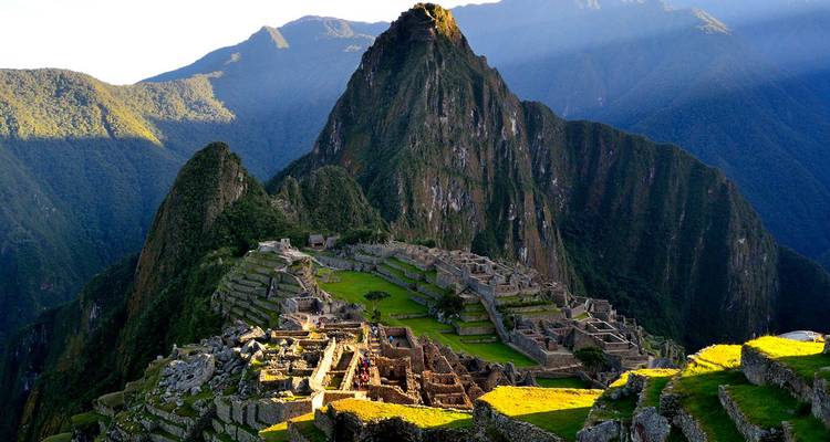 Ikonischer Blick auf die Ruinen von Machu Picchu, die auf einem grünen Bergsattel thronen, mit dramatischen Andengipfeln im Hintergrund im Licht des späten Nachmittags.
