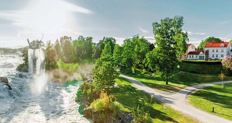 Malerischer Park mit einem Wasserfall und traditionellen europäischen Gebäuden.