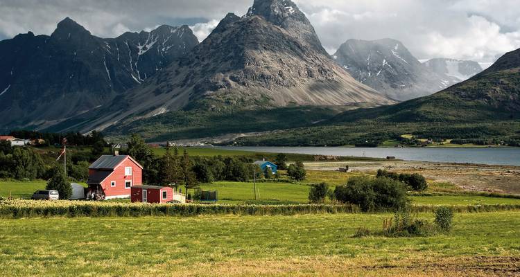 Une belle maison rouge dans un champ avec des montagnes spectaculaires en arrière-plan.