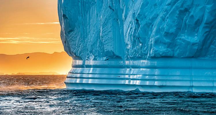 Close-up of a giant iceberg with sunset light and ocean waves.