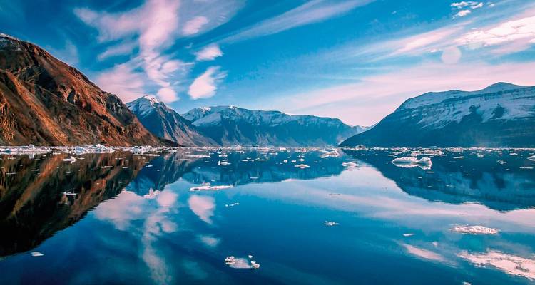 Fjord with icy waters and clear reflections of snow-capped mountains.