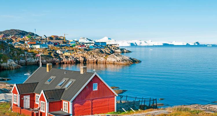 Coastal village with colorful houses near a sea filled with icebergs.