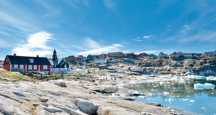 Coastal town with colorful houses and sea, mountains in the background.