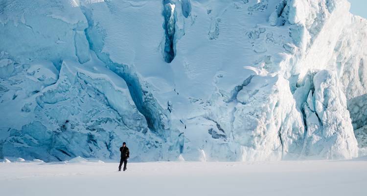 Person walking on snow in front of a large icy cliff.