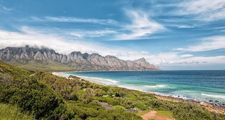 Coastal landscape with green hills and a blue ocean under a blue sky.
