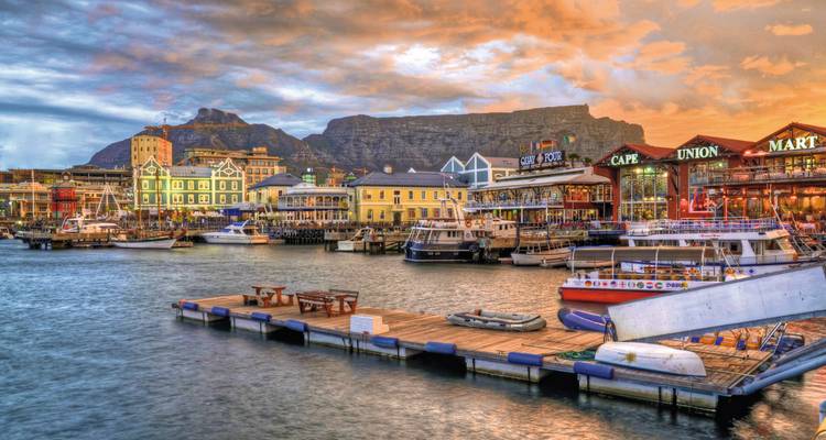 Havengebied met levendige gebouwen en boten, Tafelberg op de achtergrond tijdens zonsondergang.