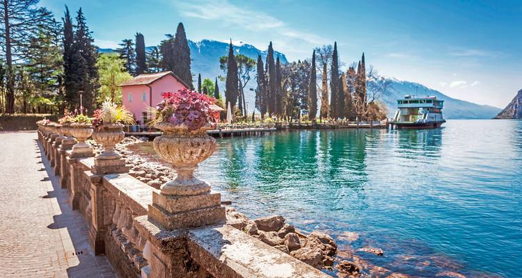 Pittoreske promenade aan het meer met verre bergen en een veerboot.