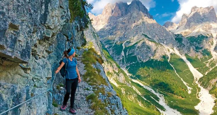Wanderer auf einem Bergpfad mit felsigen Gipfeln im Hintergrund.
